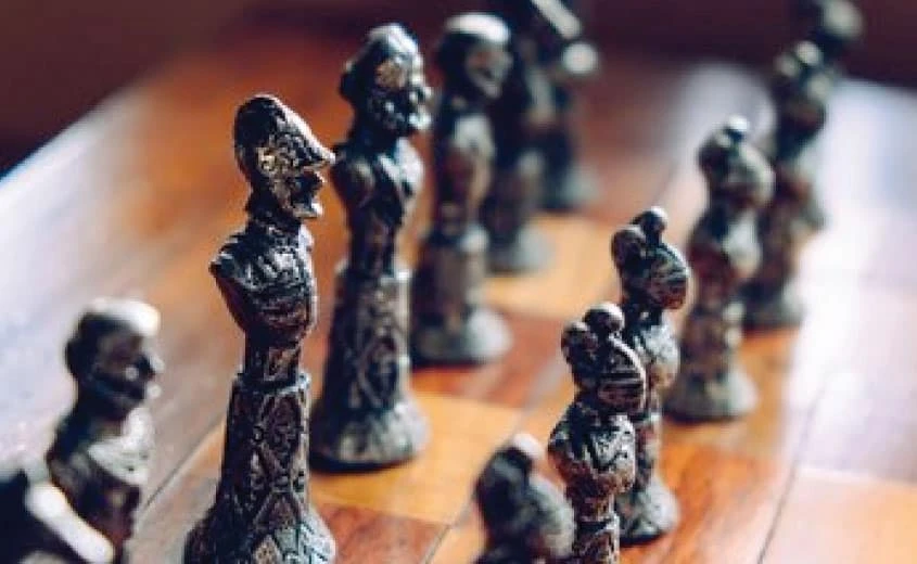 Close-up of intricately detailed metal chess pieces arranged on a wooden chessboard, with the focus on the nearest pieces and the background pieces slightly blurred.