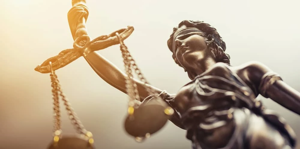 Close-up of a bronze statue of Lady Justice holding scales and a sword, with a blindfold over her eyes, symbolizing fairness and impartiality in the legal system.
