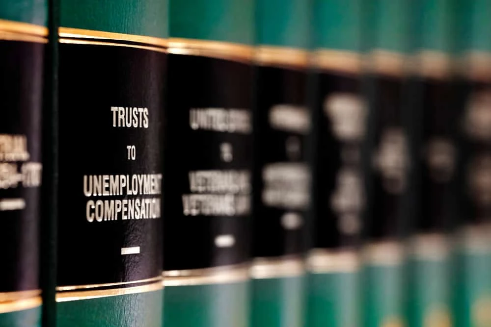 Close-up view of green hardcover law books on a shelf, with the spine of one book prominently labeled "TRUSTS TO UNEMPLOYMENT COMPENSATION" in gold and white text on a black background.