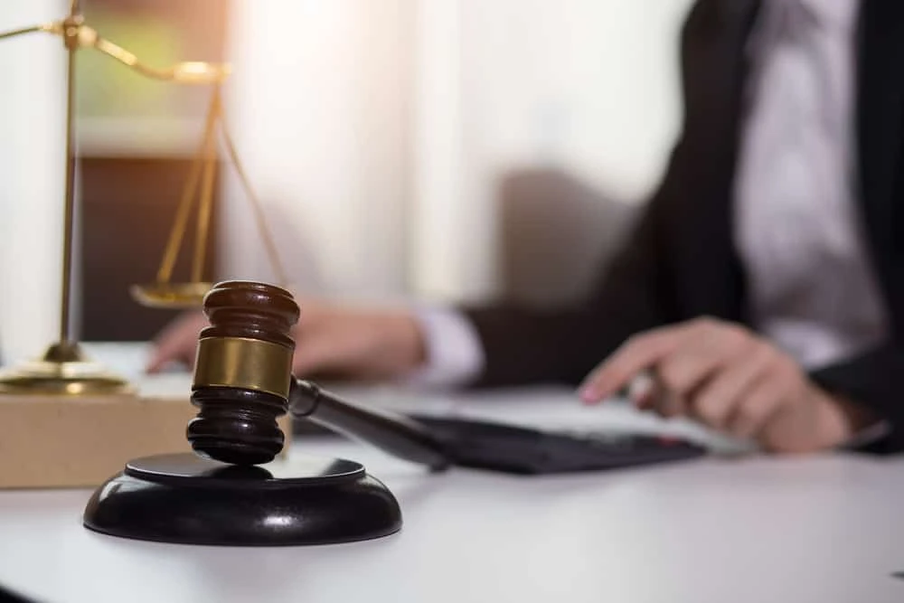 A person in a suit sits at a desk typing on a keyboard, immersed in civil litigation. In the foreground, a gavel rests on a wooden block, while a set of scales is slightly blurred in the background.